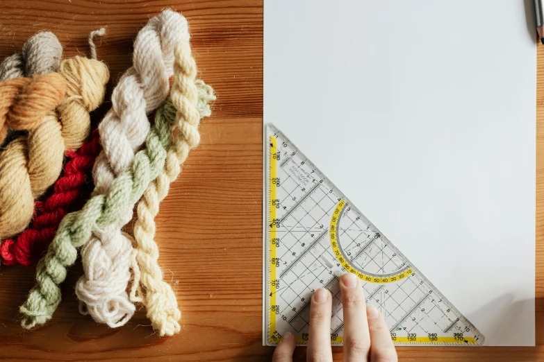 a piece of paper sitting on top of a wooden table, a cross stitch, trending on pexels, process art, holding scale, yarn, pythagorean theorem, professional product photo