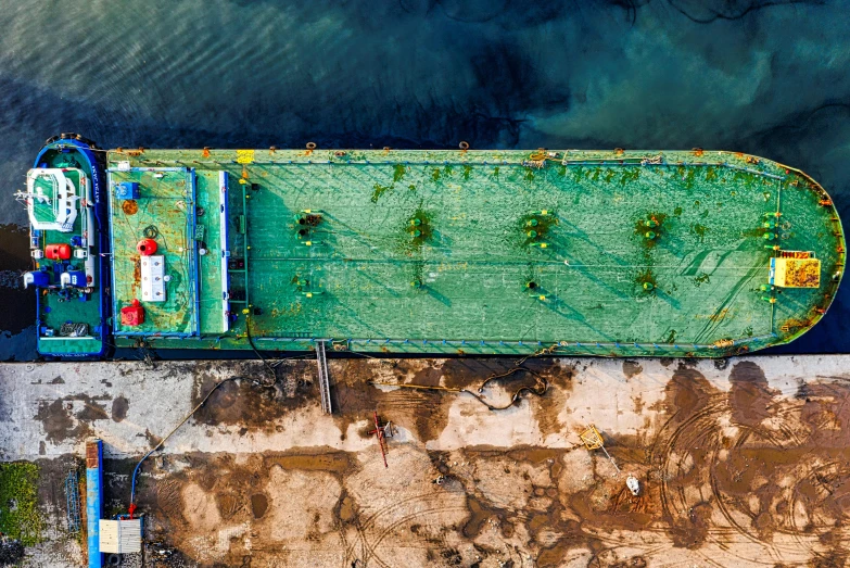 a green boat sitting on top of a body of water, unsplash contest winner, environmental art, shipping docks, made of oil and water, drone photograpghy, afar