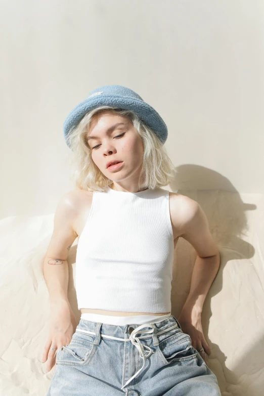 a woman laying on a bed with her eyes closed, an album cover, inspired by Elsa Bleda, white baseball hat, sleeveless turtleneck, portrait anya taylor-joy, sky blue
