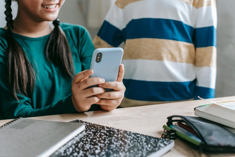 a young girl sitting at a table looking at her cell phone, trending on pexels, school class, medium shot of two characters, bottom angle, teenage boy