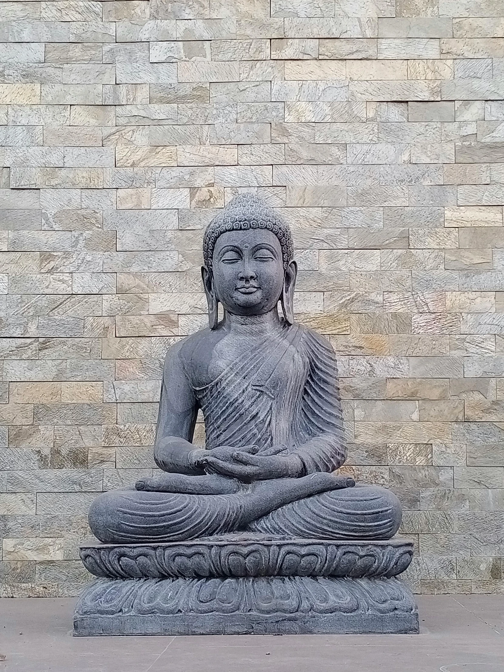 a statue of buddha sitting in front of a stone wall, photo taken in 2 0 2 0, centered full body pose, slate, puṣkaracūḍa