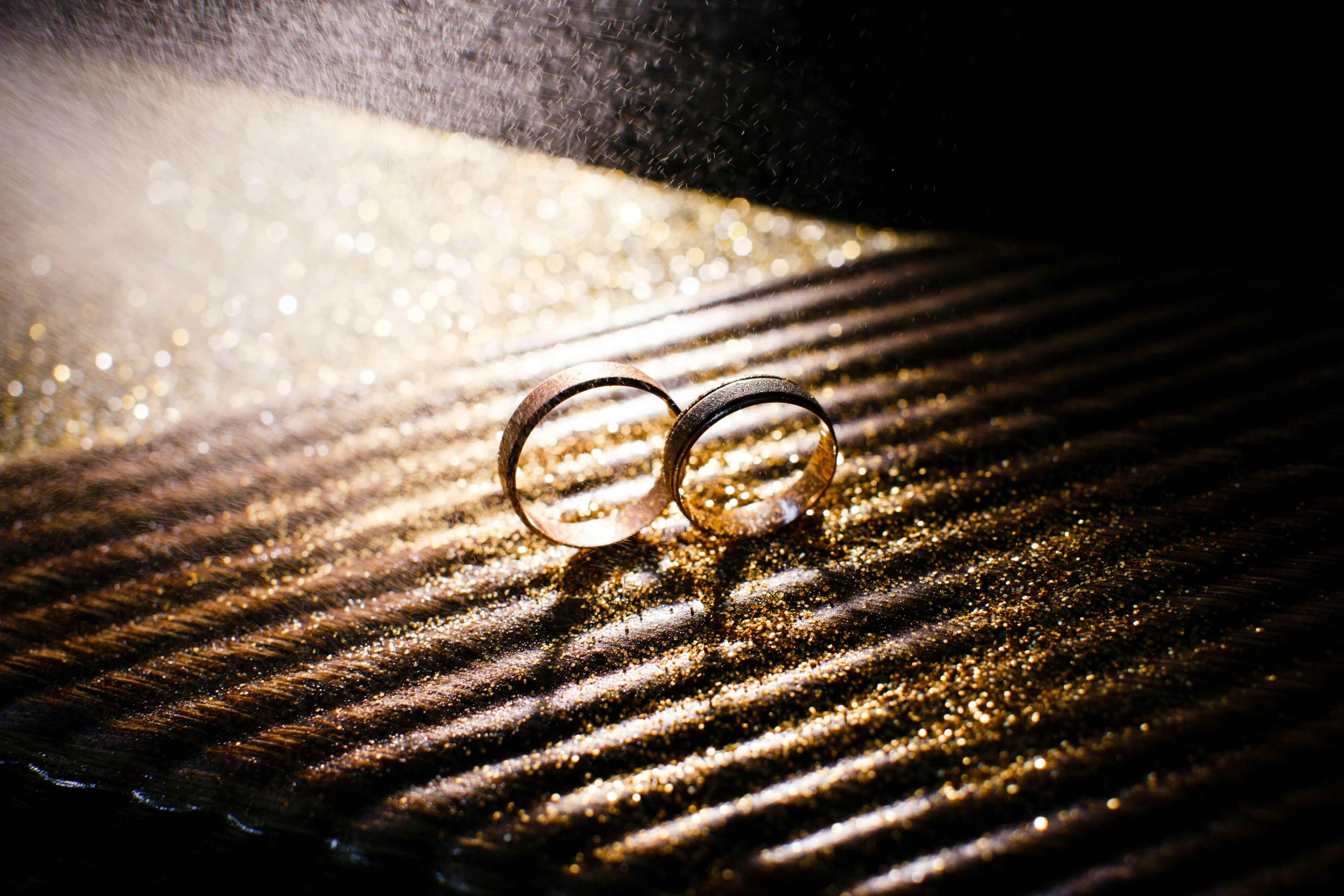 a couple of wedding rings sitting on top of a table, by Julia Pishtar, pexels, romanticism, gold dust, black and gold, ringflash, flattened