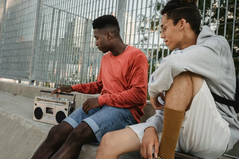 two men sitting next to each other on a bench, trending on pexels, happening, boombox, mix of ethnicities and genders, wearing a cropped top, looking at the ground
