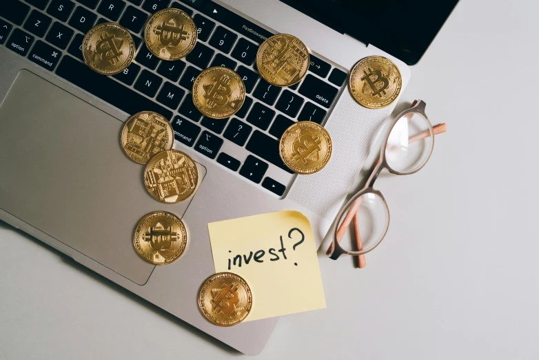 a laptop computer sitting on top of a white desk, by Adam Marczyński, pexels contest winner, art nouveau, gold coins, bitcoin, instagram post, wearing gold glasses