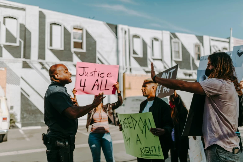 a group of people holding signs in front of a building, a photo, trending on pexels, black arts movement, police officers, people looking at a house, justice, standing on street corner