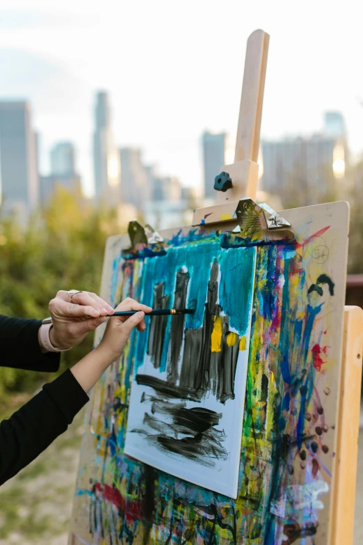 a woman painting on an easel with a cityscape in the background, multiple brush strokes, al fresco, skyline, see