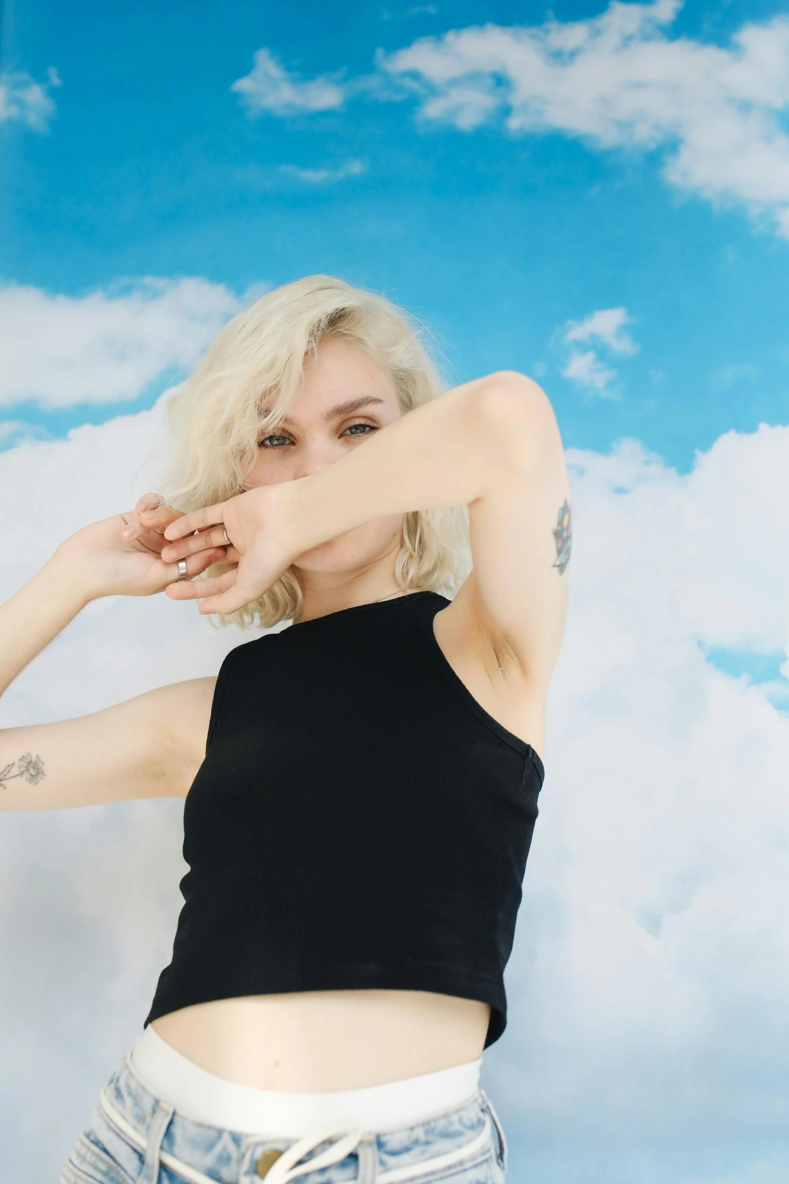 a woman posing for a picture in front of a cloudy sky, an album cover, inspired by Elsa Bleda, pexels contest winner, photorealism, pale hair, arms out, solid background, with tattoos