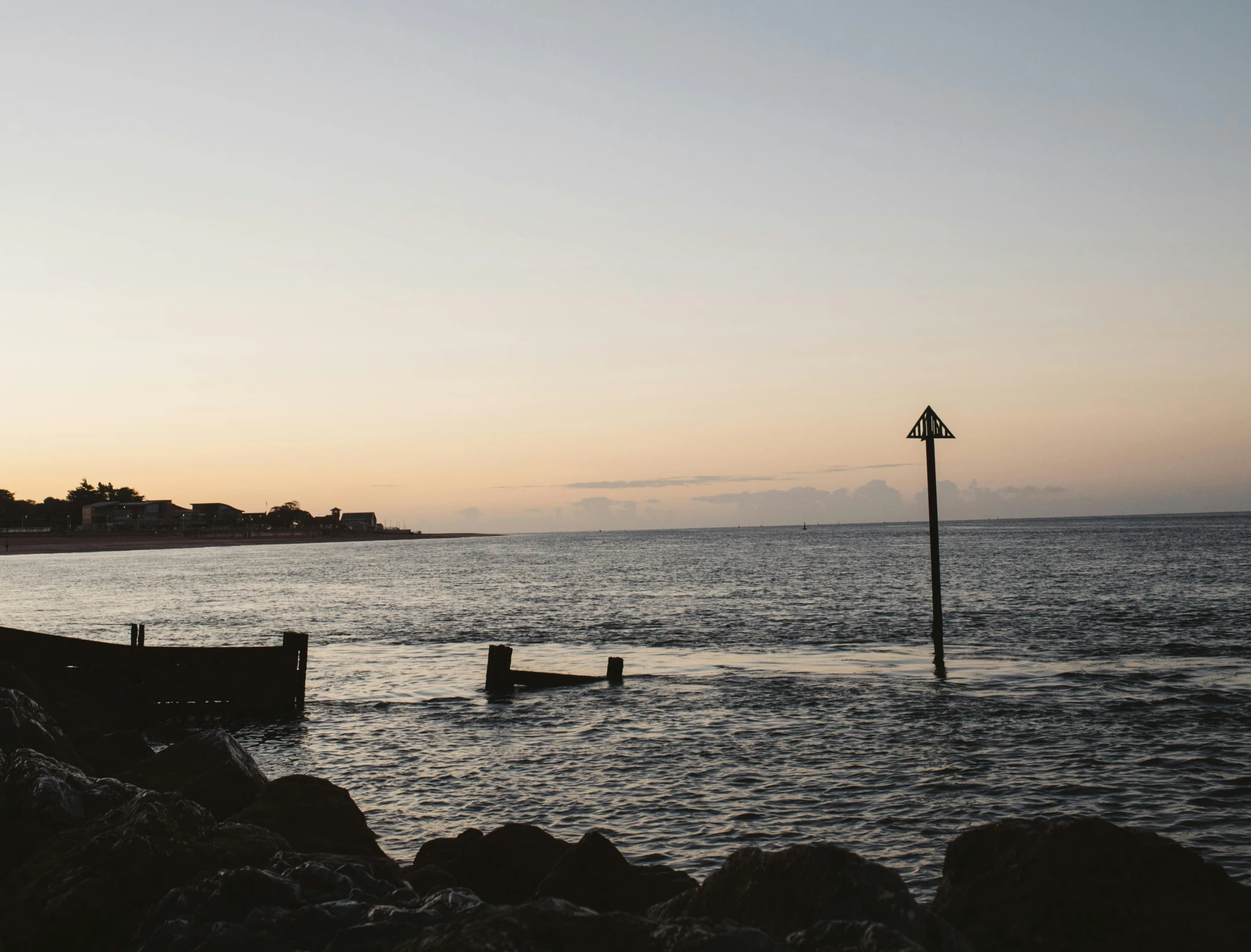 a man standing on top of a beach next to a body of water, a picture, unsplash, happening, maryport, humid evening, near a jetty, sunken