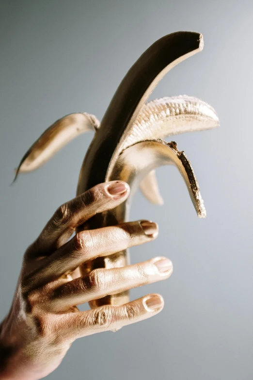 a person holding a banana in their hand, a surrealist sculpture, inspired by Elsa Bleda, trending on unsplash, renaissance, gold and white, tusks, grain”, made of bronze