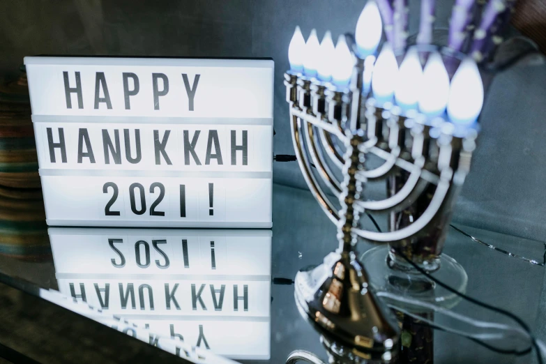 a menorah sitting on top of a table next to a sign that says happy hanukkah, pexels, hurufiyya, new years eve, instagram post, neon electronic signs, k