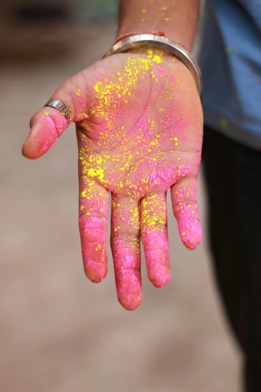 a person with yellow and pink paint on their hands, full of sand and glitter, heavy pigment, deep colour, handheld