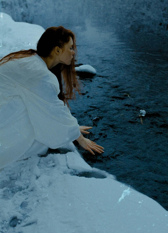 a woman sitting on top of snow covered ground next to a body of water, inspired by Elsa Bleda, pexels contest winner, symbolism, galadriel in lothlórien, crossing the river, vhs colour photography, movie still from the matrix