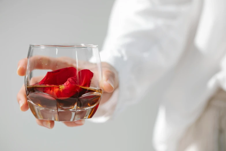 a close up of a person holding a glass of wine, large individual rose petals, whisky, wearing a white button up shirt, infused