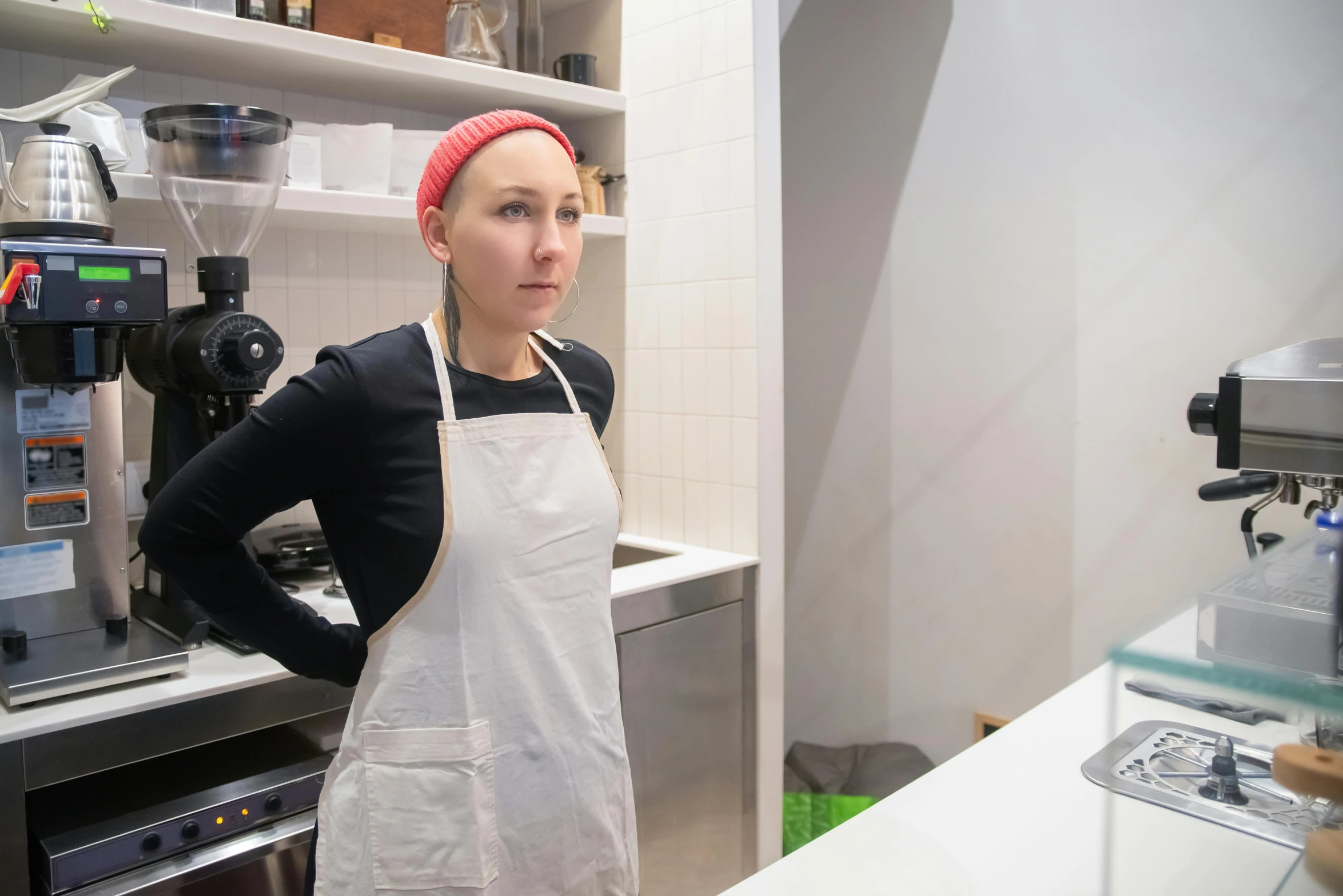 a woman standing in a kitchen next to a coffee machine, a portrait, by Liza Donnelly, unsplash, process art, dressed as a pastry chef, porcelain holly herndon statue, looking from shoulder, sydney hanson