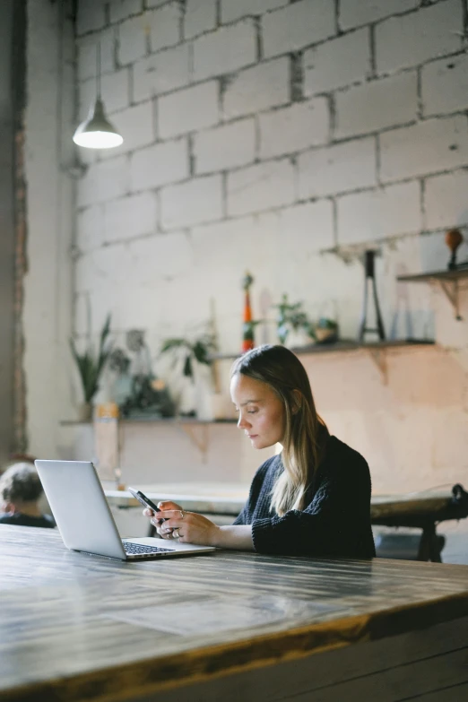 a woman sitting at a table using a laptop, trending on pexels, serious expression, low quality photo, in a workshop, gif