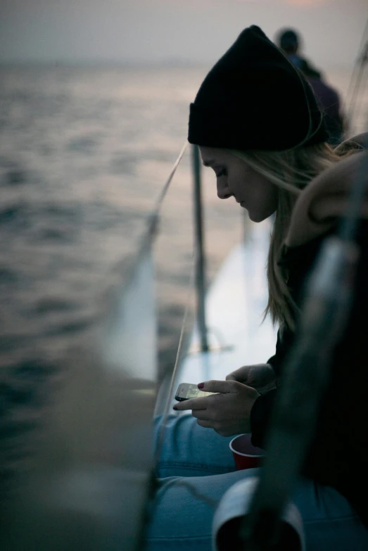 a woman sitting on a boat looking at her cell phone, by Niko Henrichon, trending on unsplash, romanticism, sad man, chilly dark mood, reflection of phone in visor, sittin