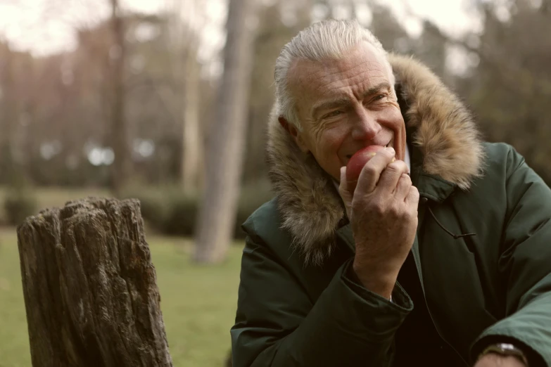 a man in a parka eating an apple, a photo, inspired by Werner Andermatt, pexels, geralt of rivia, geert wilders, warm smile, old color photograph