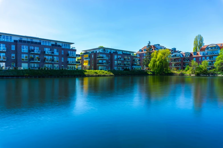 a body of water with a bunch of buildings in the background, by Sebastian Spreng, unsplash, esher, carrington, lake blue, apartment