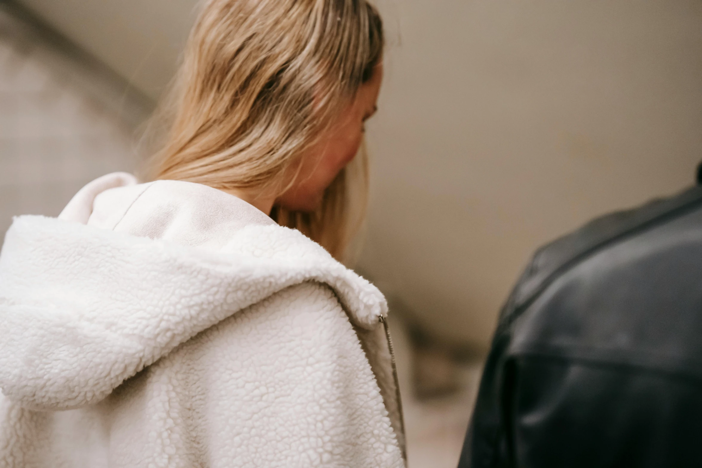 a woman in a white robe standing next to a man in a black jacket, by Emma Andijewska, trending on pexels, happening, beige hoodie, half turned around, close up of a blonde woman, wearing shoulder cape