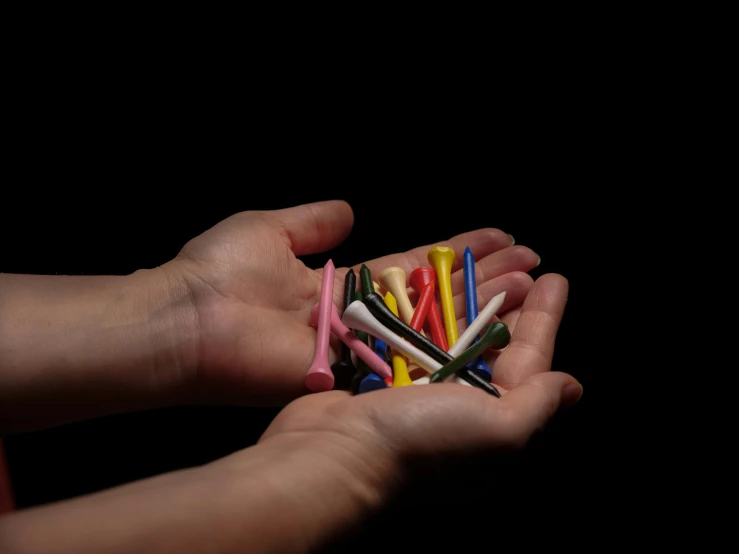 a person holding a bunch of crayons in their hands, by Doug Ohlson, on black background, tiny sticks, eleven from stranger things, clay amulets