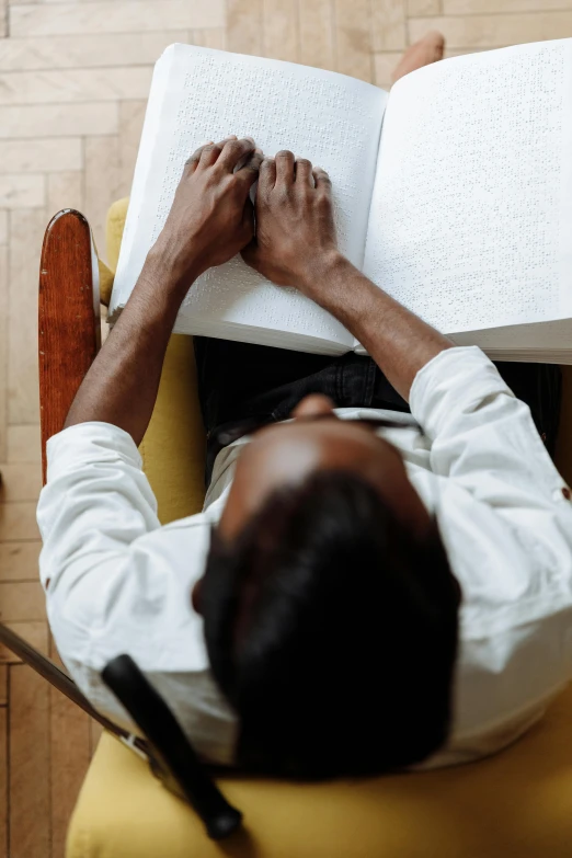 a man sitting in a chair reading a book, by Carey Morris, pexels contest winner, black man, top-down shot, on a white table, pray