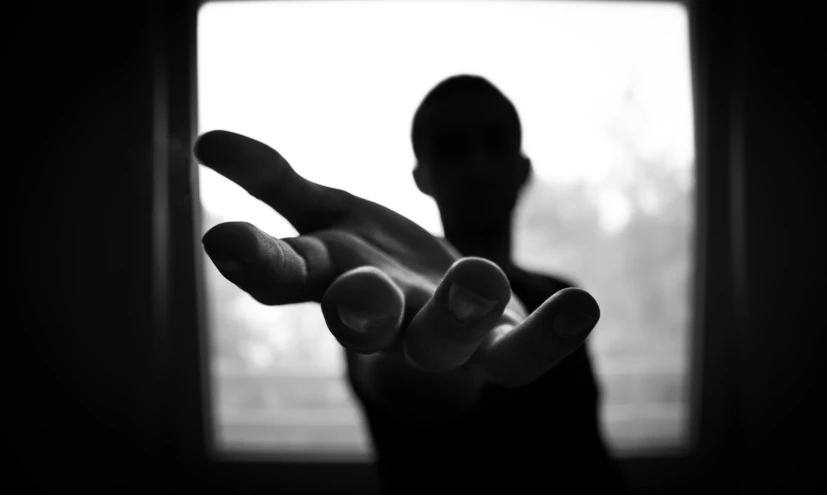 a person holding their hand out in front of a window, a black and white photo, visual art, fighting pose, uploaded, shadow people, holding