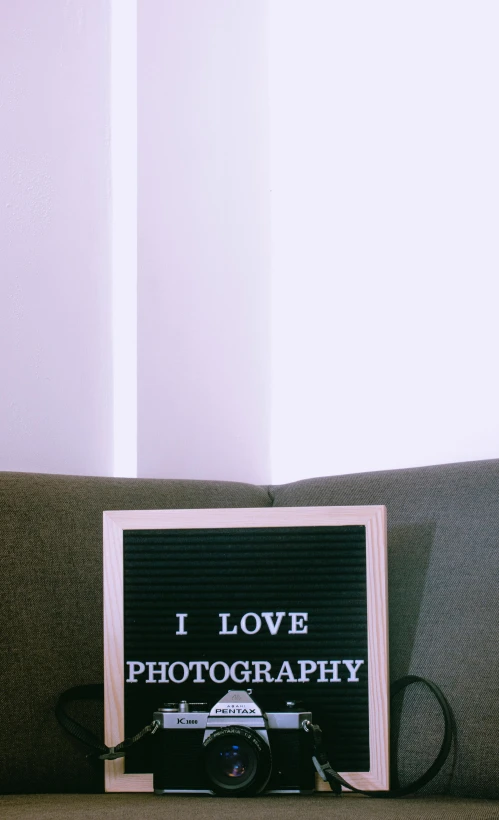 a camera sitting on top of a couch next to a sign that says i love photography, by Carey Morris, unsplash contest winner, ascii art, apprehensive mood, fully in frame, casually dressed, whiteboard