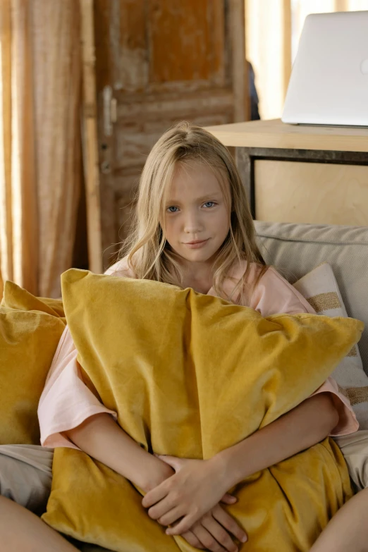 a little girl sitting on top of a couch covered in pillows, pexels, yellow robes, aged 13, ochre, disappointed