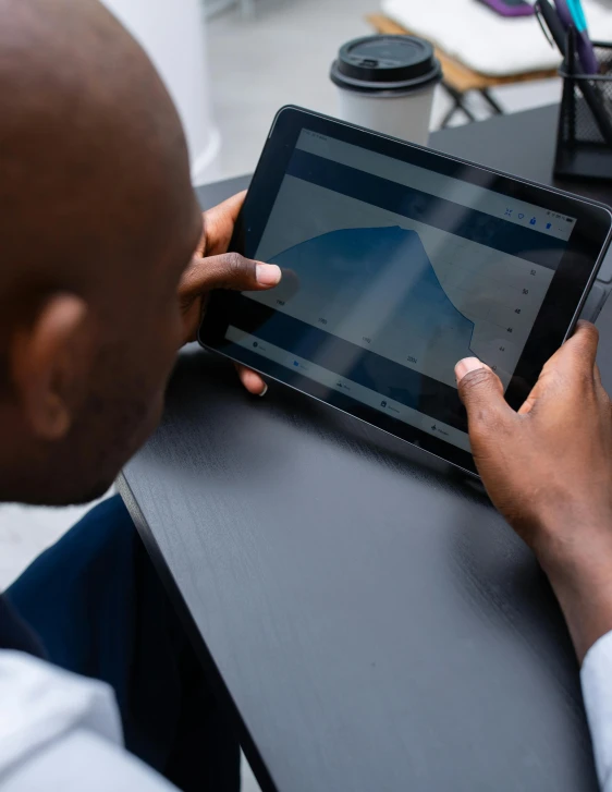 a man sitting at a desk using a tablet computer, by Carey Morris, trending on unsplash, panel of black, lgbtq, high angle shot, data visualization