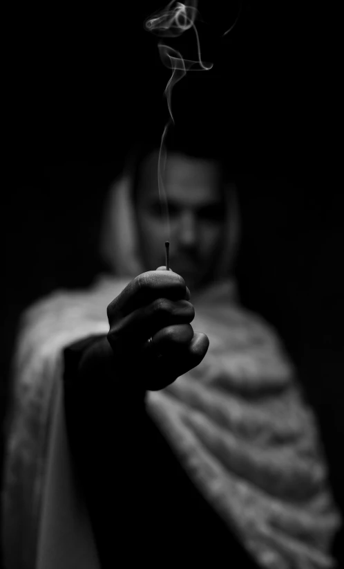 a man holding a cigarette in his hand, by Ibrahim Kodra, candle, monochrome:-2, priestess, spear in hand