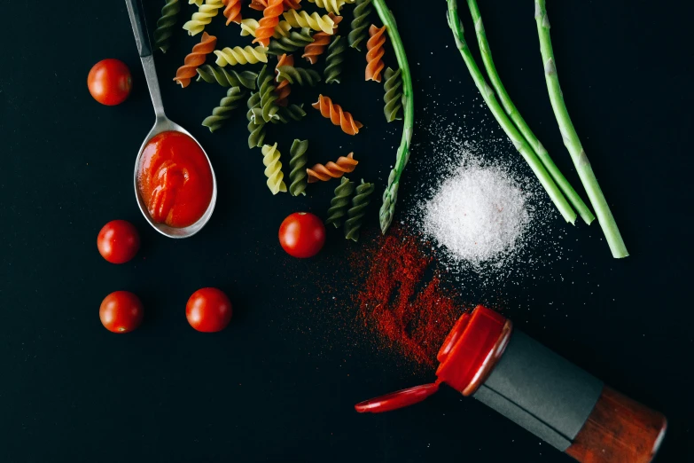 a table topped with pasta, asparagus and tomatoes, by Julia Pishtar, pexels contest winner, process art, salt shaker, red on black, spatula, close-up product photo