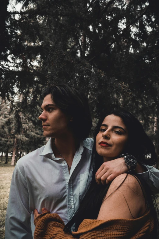 a man and a woman standing next to each other, by Lucia Peka, pexels contest winner, with long dark hair, trees in the background, non binary model, cindy avelino