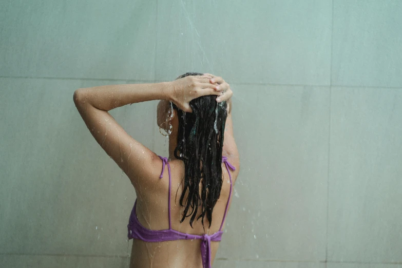 a woman in a purple bikini standing in a shower, pexels contest winner, her hair is tied above her head, back of the hair, rain and thick strands of mucus, young woman in her 20s