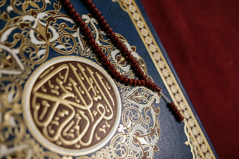 a close up of a book with a rosary on it, hurufiyya, gold and red filigree, praise the omnissaiah, navy, thumbnail