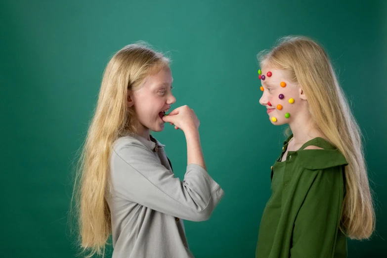 a couple of young girls standing next to each other, inspired by Damien Hirst, interactive art, bumpy nose, product introduction photo, eating, green facemask