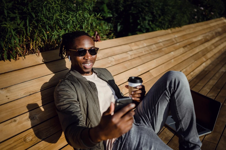 a man sitting on a bench holding a cup of coffee, trending on pexels, happening, implanted sunglasses, avatar image, man is with black skin, instagram photo