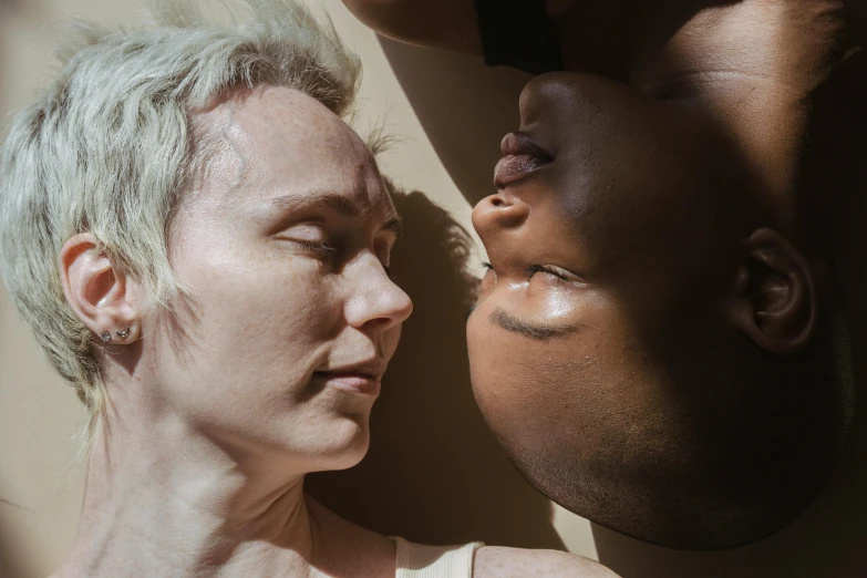 a woman laying on top of a bed next to a baby, by Sophia Beale, unsplash, hyperrealism, close - up of the faces, in the sun, non-binary, portrait of ororo munroe