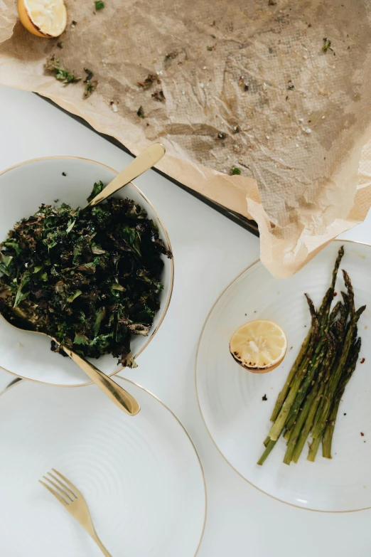 a table topped with plates of food and silverware, unsplash, dried herbs, asparagus, foil, lush greens