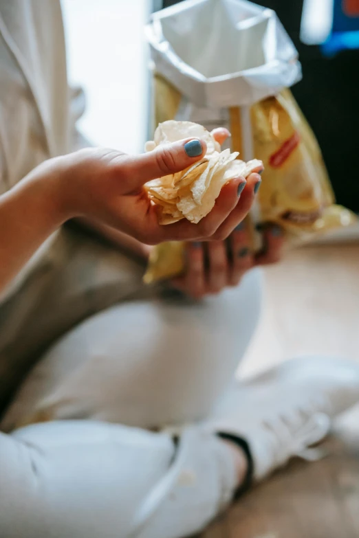 a woman sitting on the floor holding a bag of chips, pexels, process art, butter, someone sits in bed, ruffles, closeup at the food