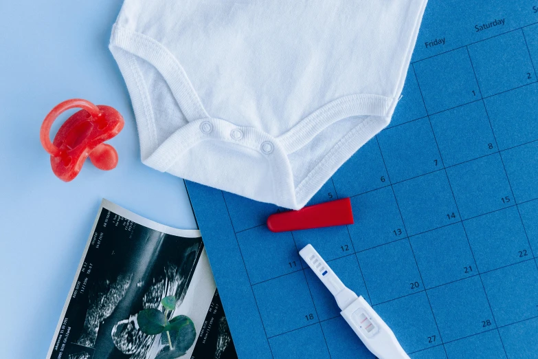 a white bodysuit sitting on top of a blue sheet of paper, pexels contest winner, crafts and souvenirs, blueprint red ink, medical supplies, pregnancy