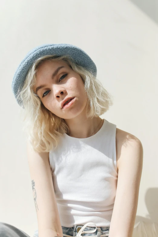 a woman sitting on the ground wearing a hat, an album cover, inspired by Elsa Bleda, featured on reddit, minimalism, pastel hair, sydney sweeney, hand holding cap brim, white and blue