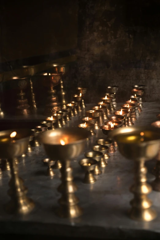 a bunch of candles that are on a table, underground temple, brass, serene lighting, medium-shot