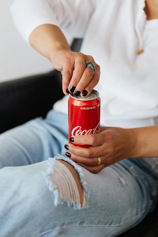 a woman sitting on a couch holding a can of coke, trending on unsplash, 👅 👅, on a white table, metallic red, good light