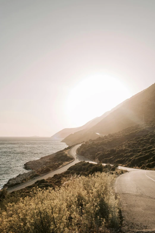 a person riding a motorcycle down a road next to the ocean, unsplash contest winner, minimalism, hollister ranch, golden hour sun, steep cliffs, greece