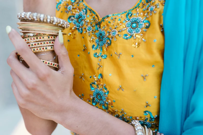 a close up of a person holding a cell phone, yellow ornate dress, gold and teal color scheme, blue colored traditional wear, golden and silver jewerly