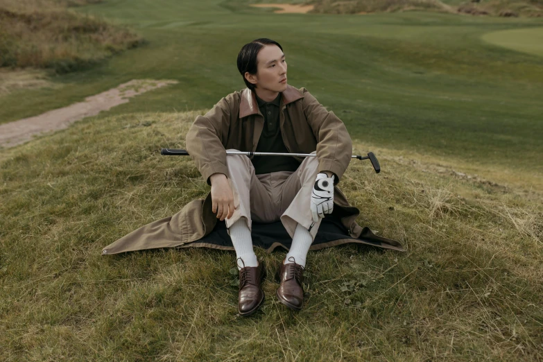 a woman sitting on top of a grass covered field, a portrait, inspired by Fei Danxu, unsplash, golf course, wearing a brown leather coat, androgynous male, avatar image