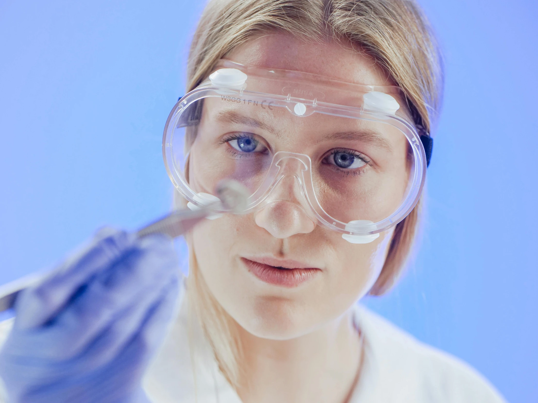 a woman in a lab coat and goggles holding a pair of scissors, by Adam Marczyński, pexels contest winner, hyperrealism, sleek oled blue visor for eyes, hd footage, microscopic view, blue