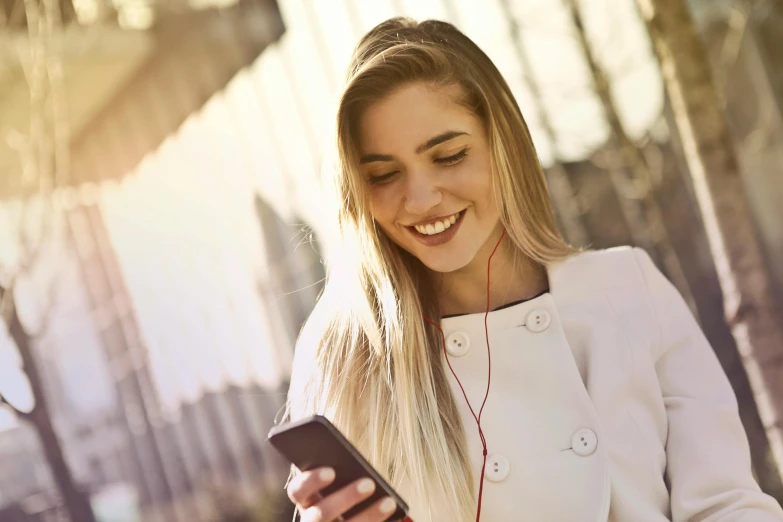 a close up of a person holding a cell phone, she is smiling, in the sun, a girl with blonde hair, listening to music