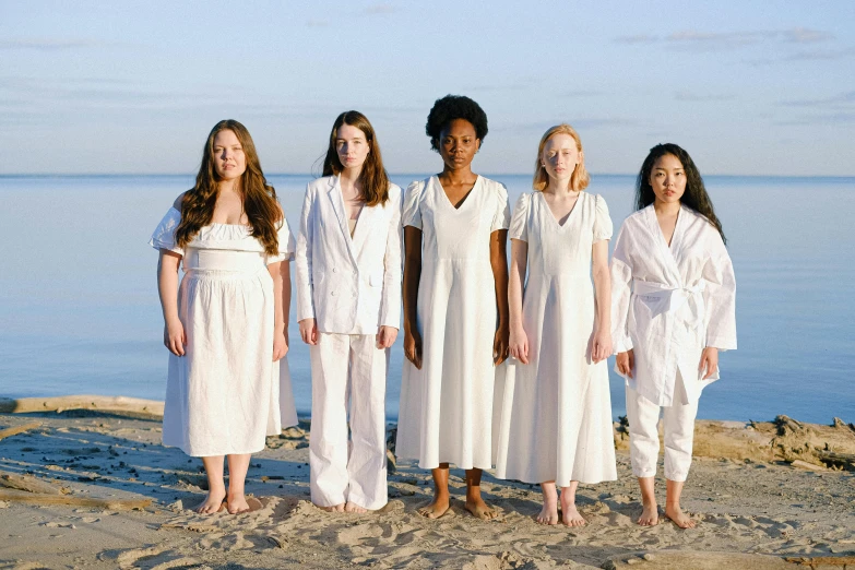 a group of women standing on top of a sandy beach, inspired by Vanessa Beecroft, unsplash, feminist art, wearing a white hospital gown, sadie sink, natural complexion, saoirse ronan