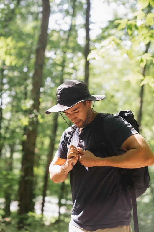 a man standing in the woods looking at his cell phone, black sun hat, asher duran, climber, profile image